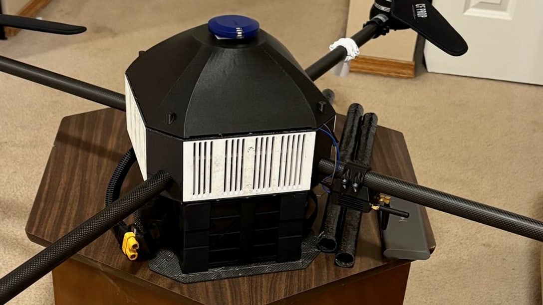 Close on the centre body: the printed dome over the avionics stack, the antenna masts, and the carbon arms clamped between the plates