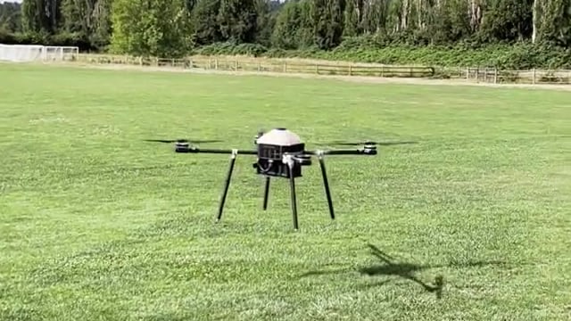 The quadcopter holding a low hover a metre above the grass, its shadow directly beneath it